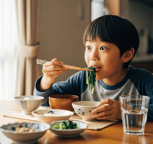お箸で緑の野菜を驚きながらも美味しそうに食べる男の子